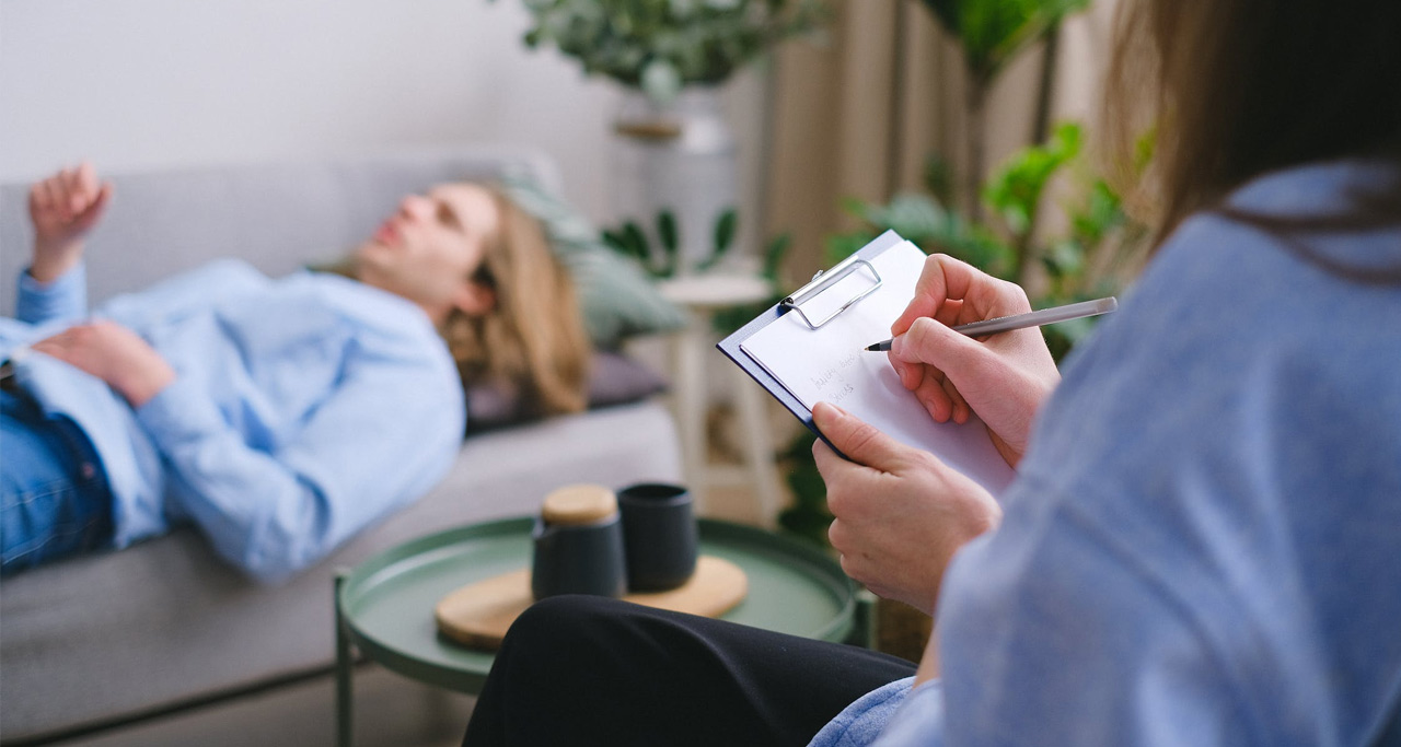 Paciente deitado, sendo tratado por um psiquiatra escrevendo em uma prancheta.
