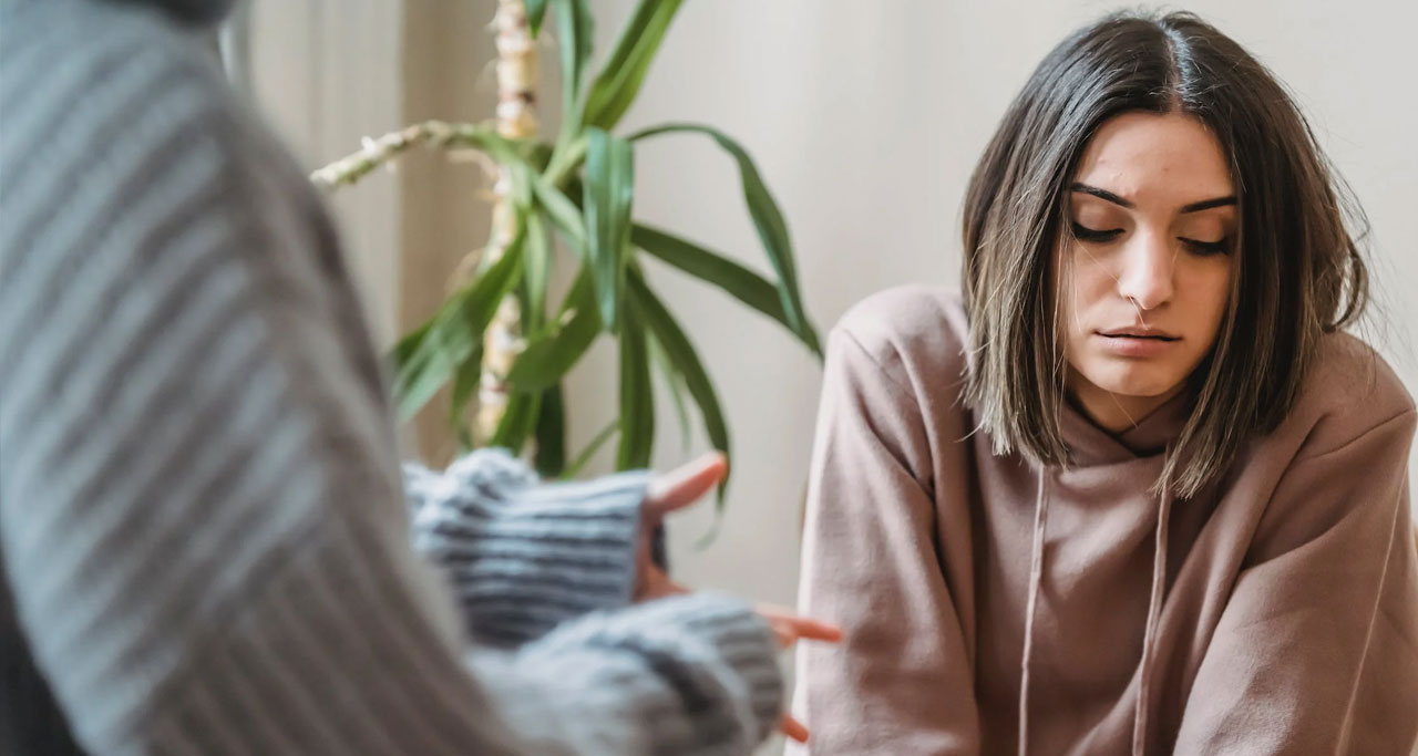 Mulher de cabelo curto séria, vestida com um casaco bege, com aparência de triste.
