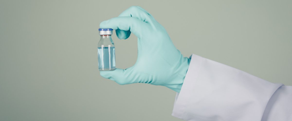 médico com luva verde segurando remédio em vidro transparente