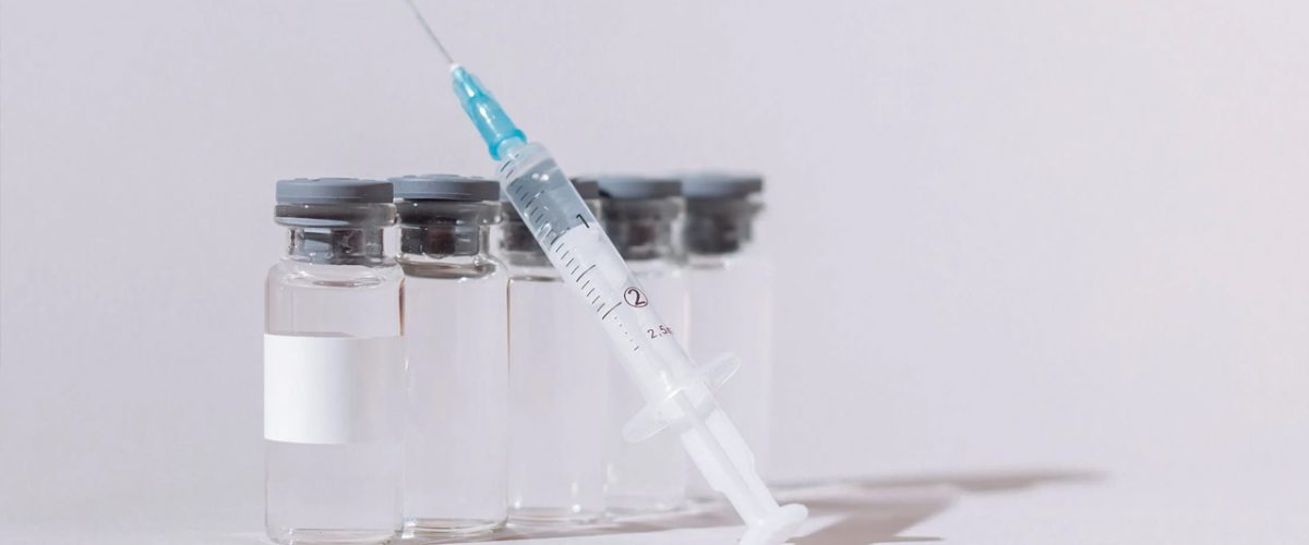 Imagem de seringa e embalagens de remédio, feitas de vidro.