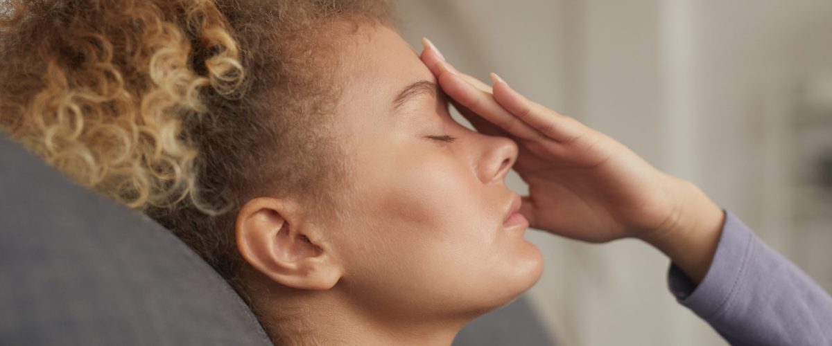 depressao-endogena Mulher de olhos fechados, com a mão tocando o centro da testa, numa expressão de cansaço.