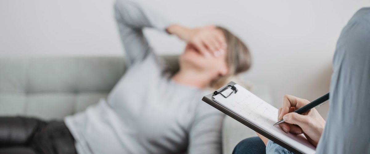 diagnostico-de-depressao Paciente deitada em um sofá, enquanto seu psiquiatra faz anotações na prancheta durante um diagnóstico de depressão.