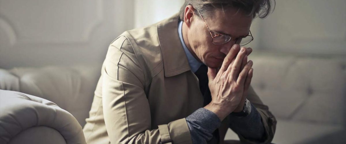 Homem vestido com blusa bege encosta as mãos uma na outra, como se tivesse preocupado.