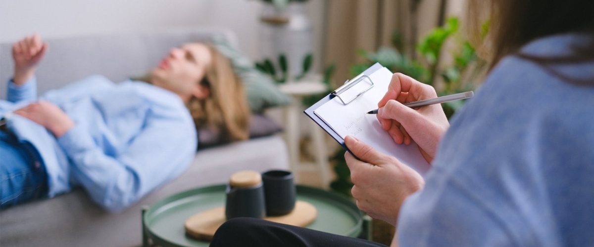 quem trata depressão Paciente deitado, sendo tratado por um psiquiatra escrevendo em uma prancheta.