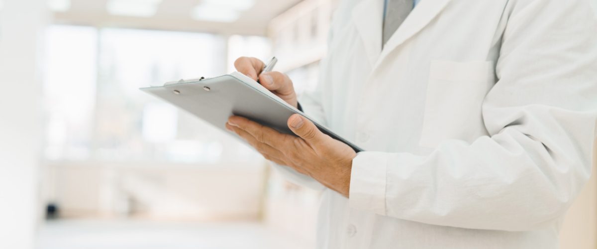 spravato Médico escrevendo uma prancheta. Ele está em pé, no corredor de uma clínica.